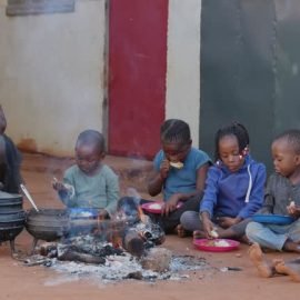 Poverty in Africa. Hungry Black African children sitting around a fire eating corn/maize and chicken